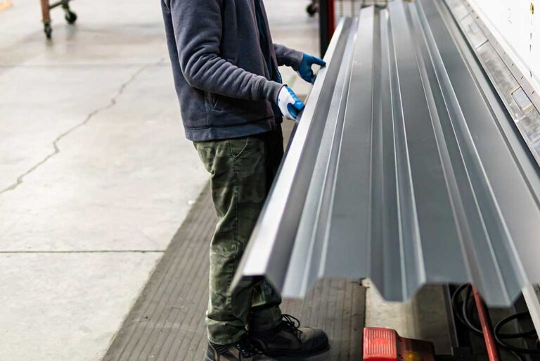 Close-up of a gloved person inspecting flashing and sealant around a plumbing vent on a shingled roof.