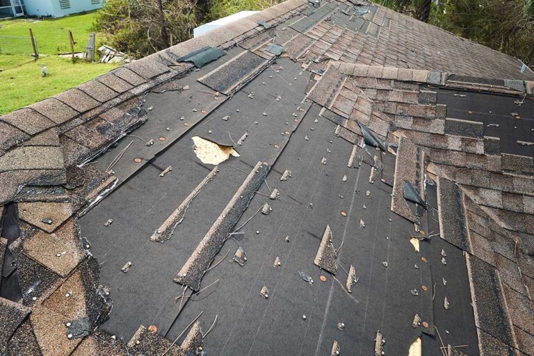 Person inspecting curled roof shingles and a stained attic ceiling after seasonal weather.