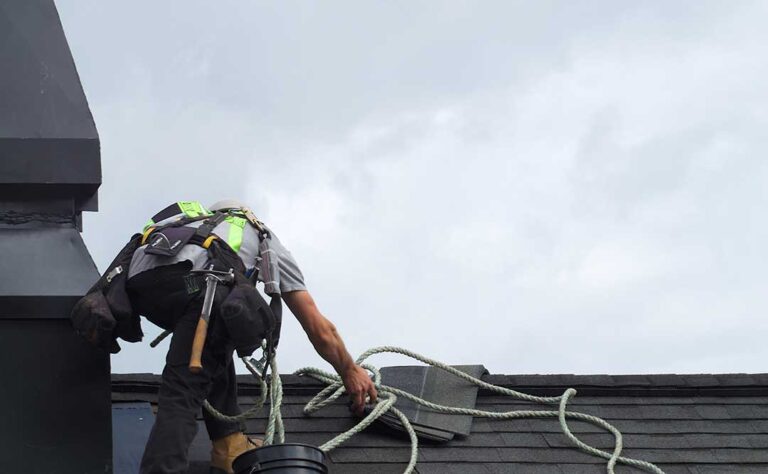 Homeowner reviews roofing warranty papers beside a window while roof inspection photos and repair records lie on a table.