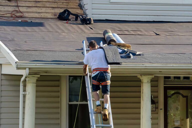 A homeowner photographs a roof leak from indoors while a worker secures a tarp outside.