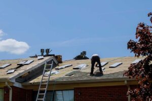Homeowner examining a ceiling water stain beneath a roof with visible damaged shingles and wet attic insulation.